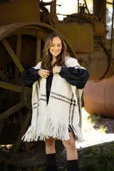 Ruana artesanal de lana merino en color crudo con detalles de líneas horizontales en color marrón chocolate y terminación con flecos en el ruedo.