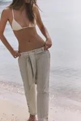 Pantalón de tiro medio con estampado de rayas verticales, confeccionado en mezcla de lino. Presenta trabillas, cinturón del mismo tejido para anudar en la cintura, cierre frontal con cremallera y botón, y detalle de abertura con botones en el bajo.