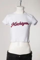Remera baby tee blanca de morley, con ajuste al cuerpo, mangas cortas, cuello redondo y estampado con la inscripción 'Michigan' en estilo college.