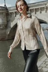 Camisa de manga larga con cuello solapa, confeccionada en tejido satinado con textura efecto arrugado y cierre frontal con botones dorados.