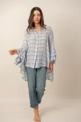 Camisa de manga larga con diseño a cuadros en tonos celestes, marrones y blancos. Presenta corte asimétrico con largo irregular, más larga en la parte trasera, y mangas amplias con volados escalonados.