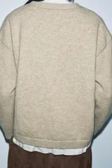 Chaqueta tipo cárdigan de lana en color beige, con diseño de tejido combinado que incluye una capa interior de tela clara. Presenta escote en pico, manga larga y cierre frontal con botones oscuros.