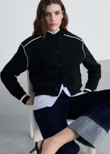 Chaqueta estilo bomber de tejido de punto en color negro, con cuello redondo, cierre frontal de botones y detalles de rayas blancas en contraste en los hombros y puños.