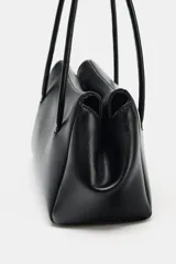 Bolso de hombro negro de formato alargado en símil cuero, con doble asa fina, cierre imantado y bolsillo interior con cremallera.