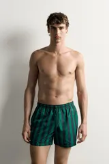 Short de baño confeccionado en tejido técnico, con diseño de rayas verticales en color verde y negro. Cuenta con cintura elástica ajustable con cordón, bolsillos laterales y bolsillo trasero con vivo, además de forro interior.