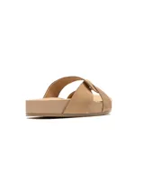 Sandalias tipo slide color tostado con tiras cruzadas de cuero y base plana de plataforma.
