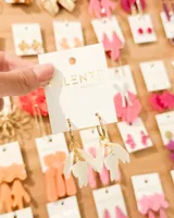 Aros tipo argolla de acero dorado con dijes colgantes en forma de pétalos o alas de resina blanca traslúcida.