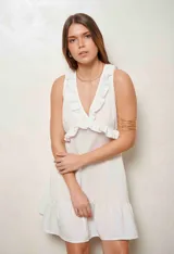 Vestido corto blanco con escote en V profundo, detalles de volados en el escote y en el ruedo, de corte sin mangas.