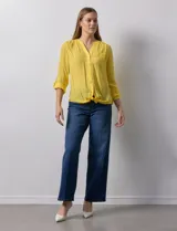 Blusa blanca de gasa marca Zac & Rachel, con cuello a la base, escote en V, abertura central con botones, bolsillo aplicado en el pecho y mangas largas regulables con presilla y botón. Tiene terminación opcional de nudo en el ruedo.