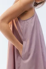 Vestido maxi solero amplio y largo de color amarillo, con escote redondo, frunces que otorgan vuelo, breteles finos ajustables con nudo en los hombros y bolsillos laterales.