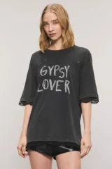 Remera oversize de jersey de algodón en color negro con efecto gastado, cuello redondo y mangas cortas. Presenta roturas distribuidas, estampa frontal con la inscripción "GYPSY LOVER", detalles de tachas y apliques de puntilla en las mangas y el ruedo.