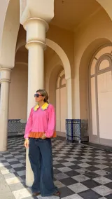 Camisa de manga larga en color rosa, con cuello Peter Pan en color amarillo y detalle de volados en los bordes. Presenta cierre frontal con botones y puños elásticos con detalle de volados.