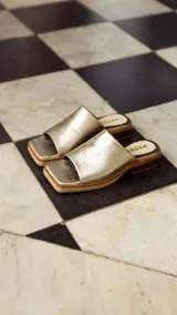 Zueco artesanal de cuero color dorado, con suela plana y taco bajo de madera con plataforma.