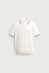 Polo de punto de algodón color blanco crudo, de corte regular fit, con cuello solapa, cierre frontal de botonadura corta y manga corta. Presenta detalles de líneas en contraste en el cuello y en los bordes de las mangas.