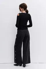 Pantalón de jean negro de corte recto y tiro alto, con detalle de botones metálicos plateados a lo largo de la costura lateral externa.
