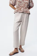 Pantalón tobillero color beige, con cintura elástica ajustable con cordones, bolsillos delanteros y falsos bolsillos con solapa en la espalda.
