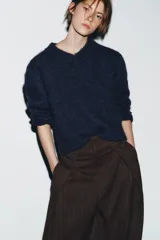 Pantalón de tiro alto con diseño tipo balloon, confeccionado en tela con estampado de rayas verticales. Presenta cintura ancha, pliegues frontales, bolsillos laterales y cierre frontal con cremallera, botón y ganchos metálicos.