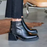Bota corta de cuero vacuno color negro, con diseño de textura croco en el talón y el taco. Presenta punta cuadrada, taco cuadrado de 6 cm y cierre lateral interno.