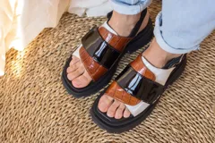 Sandalias de plataforma con suela track negra. Presentan un diseño de tiras anchas combinadas en cuero con textura de reptil color marrón y una franja central de charol negro. Incluyen una tira trasera elástica para mayor sujeción.