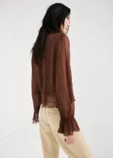 Blusa de viscosa color marrón chocolate, con diseño semitransparente, cuello alto y mangas largas con puños acampanados y volados.