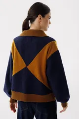 Chaqueta bomber azul marino con paneles color mostaza en forma de rombos. Tiene cuello tipo camisa, cierre frontal con cremallera, bolsillos de parche y puños y bajo acanalados en color marrón.