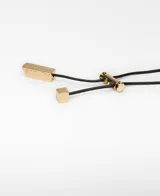 Collar con cordón largo regulable negro y gran dije metálico de forma orgánica con acabado dorado.