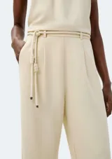 Pantalón de corte recto color beige con pinzas en la parte delantera y tira ajustable a modo de cinturón con nudos decorativos.