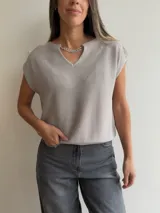 Tejido de punto de manga corta en color blanco, con escote en V y detalle de cadena metálica desmontable en el cuello. Presenta un diseño holgado y textura acanalada fina.