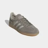 Championes Adidas Handball Spezial de diseño clásico, confeccionados en ante vacuno suave color gris con las icónicas tres tiras laterales en tono más claro. Presentan suela de goma color caramelo y cierre de cordones.