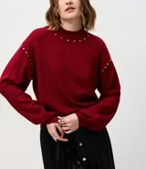 Suéter de punto color bordó con cuello alto y mangas largas con puños ajustados. Presenta aplicaciones de tachuelas metálicas decorativas en el escote y a lo largo de las mangas.