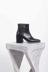 Botin de cuero y gamuza color marrón, con diseño combinado de paneles lisos y gamuzados, puntera cuadrada y taco bloque de madera con diseño geométrico. Cuenta con cierre lateral interno.