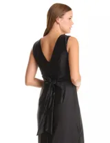 Vestido largo negro de seda fría, marca Julia Jordan. Presenta escote en V en el frente y la espalda, frunces bajo el busto y una banda ancha en la cintura con lazos largos para anudar en la espalda. La falda tiene una caída fluida con un tajo lateral pronunciado.