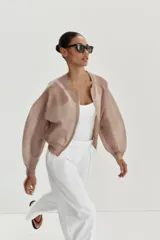 Chaqueta estilo bomber de punto color beige con acabado brillante, cuello redondo, manga larga con puños elásticos y cierre frontal con cremallera.
