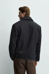 Cazadora de corte regular fit en color negro. Presenta cuello solapa con un cuello interior de punto desmontable mediante cremallera. Cuenta con cierre frontal de cremallera oculta por una solapa con botones a presión, bolsillos de plastrón con solapa en la cadera y mangas largas con puños abotonados.