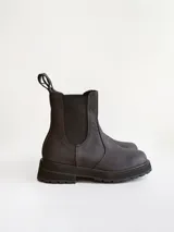 Bota tipo Chelsea de caña media, confeccionada en cuero negro con acabado mate. Presenta paneles elásticos laterales, tiradores traseros y suela track robusta con plataforma dentada.