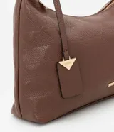 Cartera mediana tipo hobo de Satinato, confeccionada en poliuretano con textura granulada y diseño geométrico sutil. Cuenta con cierre superior de cremallera, correa de hombro ajustable y un dije decorativo metálico con forma triangular.