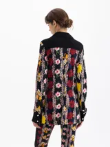 Camisa de manga larga con estampado floral sobre fondo negro. Presenta cuello, cartera de botones, puños y canesú en color negro liso. Tiene dos bolsillos plaqué con tapa en el frente, asegurados con broches metálicos negros grabados.