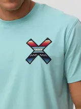Remera de algodón orgánico color blanco, con corte regular fit y detalle de bordado en forma de X con diseño geométrico multicolor en el pecho.