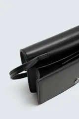 Bandolera negra con correa fina ajustable, cierre con solapa imantada, bolsillo interno y detalle de borla lateral.