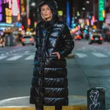 Campera puffer larga de acabado brillante, con capucha integrada, cuello alto, cierre frontal con botones a presión y puños elásticos.