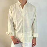 Camisa de manga larga con cuello mao, confeccionada en tejido de lino con estampado de rayas verticales en tonos amarillo y blanco. Presenta cierre frontal con botones y un pequeño bordado en el pecho.