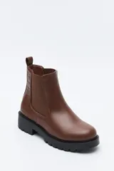 Bota tipo chelsea de caña baja con suela dentada robusta. Presenta un diseño combinado con paneles laterales elásticos, acabado liso en el frente y detalle texturizado en relieve en la parte posterior, incluyendo un tirador trasero para facilitar el calce.