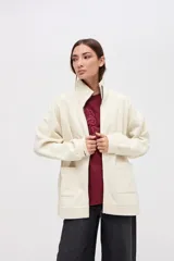 Campera oversize de felpa con friza, color crudo, con cierre metálico frontal, cuello alto y bolsillos laterales amplios. Presenta detalles de cortes en mangas y hombros, y bordado decorativo.