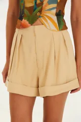 Short de tiro alto color beige con diseño de pliegues frontales y ruedo con dobladillo. Confeccionado en mezcla de viscosa y poliéster, presenta un calce fluido y bolsillos laterales.