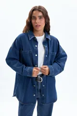Sobrecamisa de jean color azul oscuro, con corte oversize, cuello clásico, cierre frontal con botones metálicos y dos bolsillos frontales tipo parche.