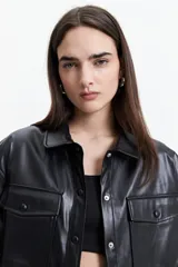 Camisa de manga corta confeccionada en cuero sintético color bordó, con cuello clásico, cierre frontal de botones metálicos y dos bolsillos frontales con solapa.