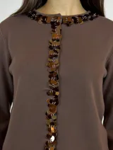 Cardigan de punto color marrón chocolate, con cuello redondo y cierre frontal de botones decorados con lentejuelas circulares brillantes. Presenta mangas largas y un corte recto.