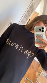 Sweater de punto negro oversize, con cuello redondo y hombros caídos, de manga larga y silueta amplia. Presenta bordado artesanal en el frente con la frase "e pur si muove" y líneas en contraste en los hombros.