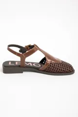 Sandalias de cuero marrón, con puntera cerrada de diseño trenzado, empeine liso y tira ajustable con hebilla en el talón. Cuenta con suela plana y baja.