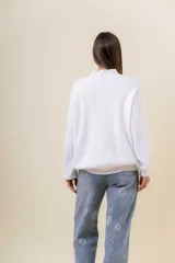Sweater tejido de punto color blanco, con cuello alto y diseño en relieve tipo chevron en la parte frontal. Presenta un calce holgado con terminaciones acanaladas en puños y ruedo.